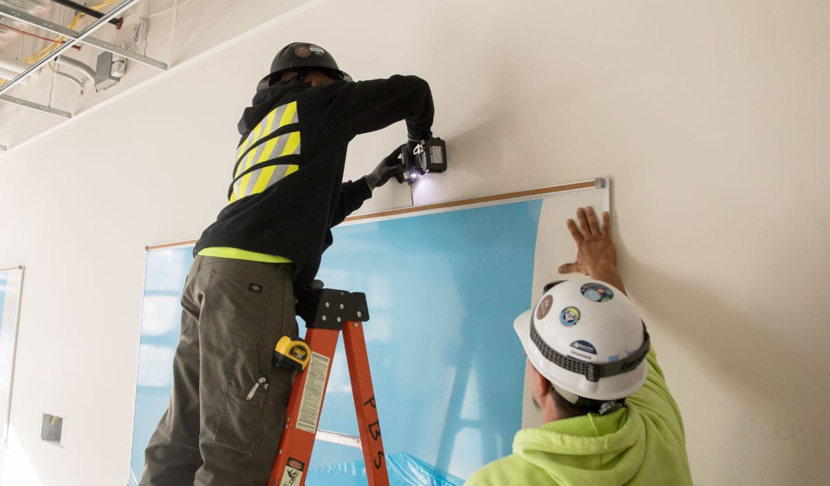 Two PBS crew members on a ladder installing a large wall graphic